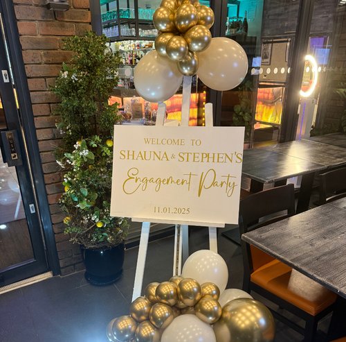 2 Gold and cream balloon display beside a personalised engagement party welcome sign