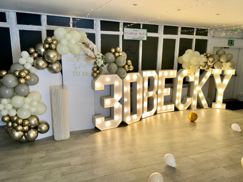 Gold light-up 30 and BECKY letters with balloon garlands at a birthday celebration