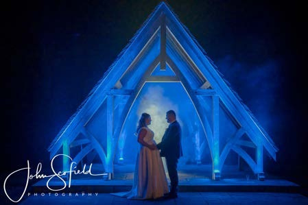 Bride and groom holding hands under a blue-lit wooden arch at Highley Manor
