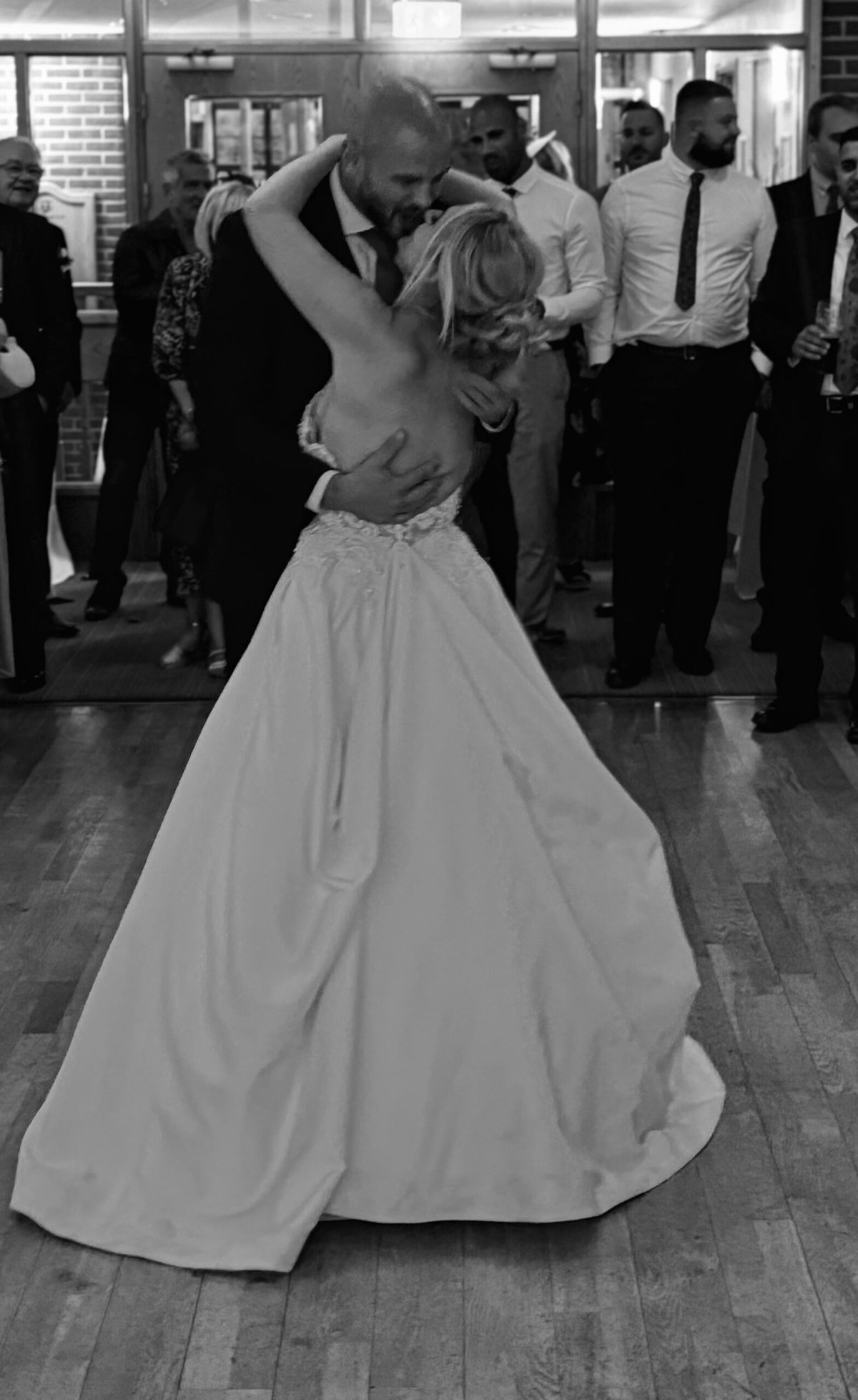 Black and white photo of a bride and groom's emotional first dance surrounded by wedding guests