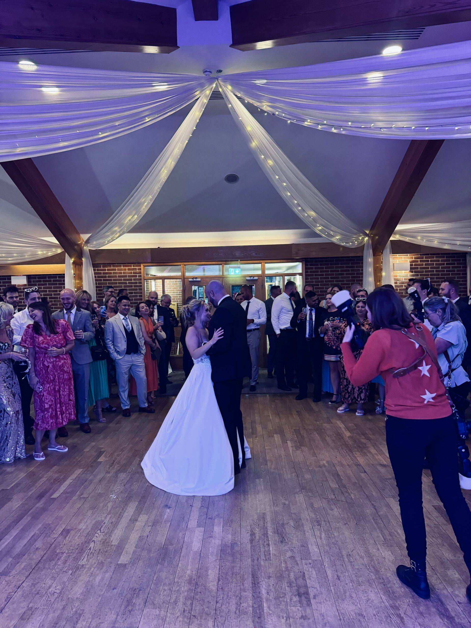 IMG_7607 Bride and groom dancing together as guests and a photographer capture the moment in a beamed reception hall