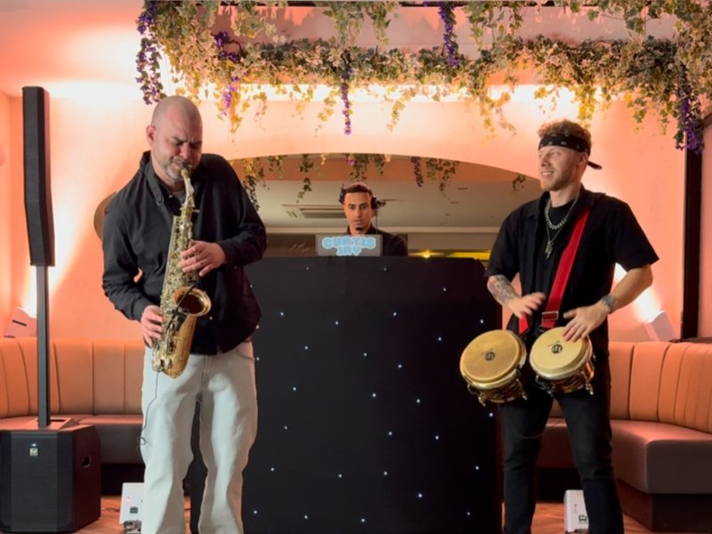 Live saxophonist and bongo player performing together in front of the DJ booth