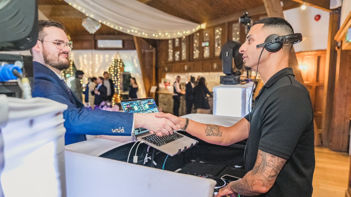 London Event DJs Curtis Jay shaking hands with a client beside the DJ booth at a barn wedding venue