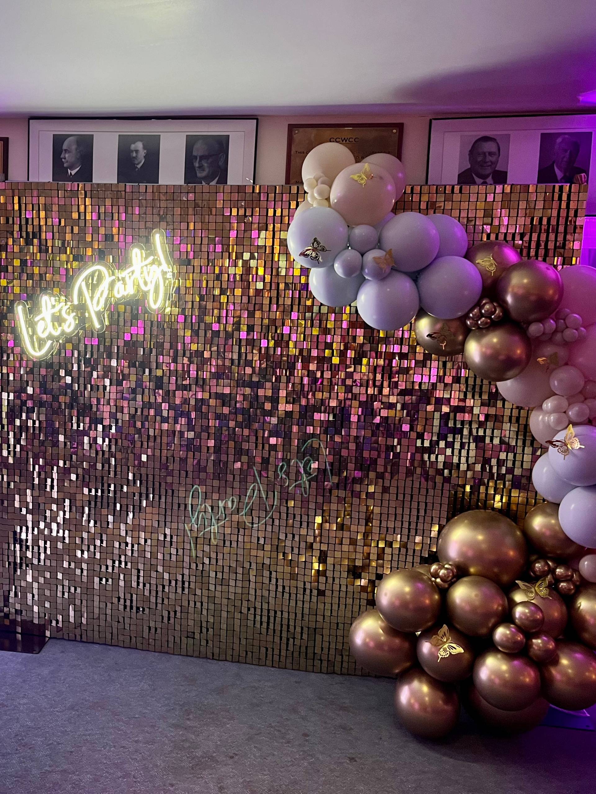Rose gold sequin shimmer wall backdrop with Let's Party neon sign and pastel balloon garland
