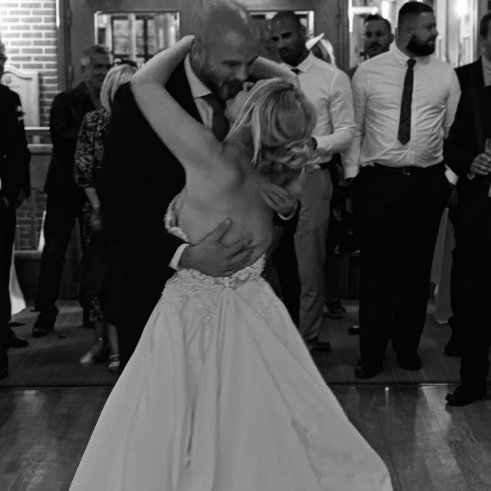 Untitled design Black and white photo of a bride and groom's first dance surrounded by wedding guests