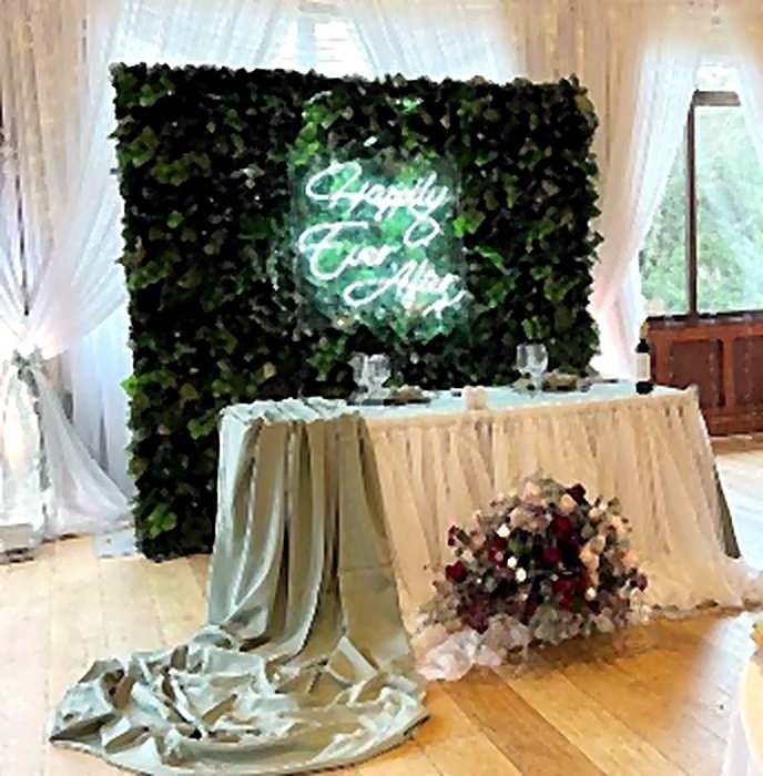 Foliage wall and neon sign behind an elegantly set sweetheart table